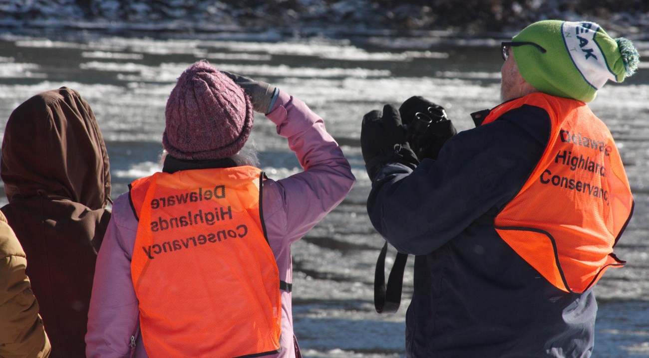 Two volunteers looking across river, facing away from camera. One holds binoculars.