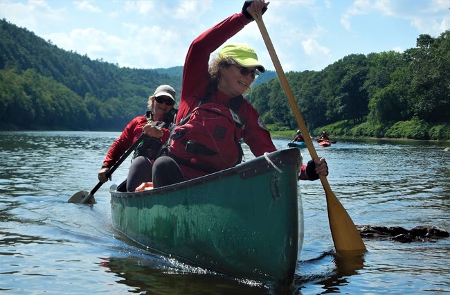Two NCSp volunteers paddling tandem in a green canoe.