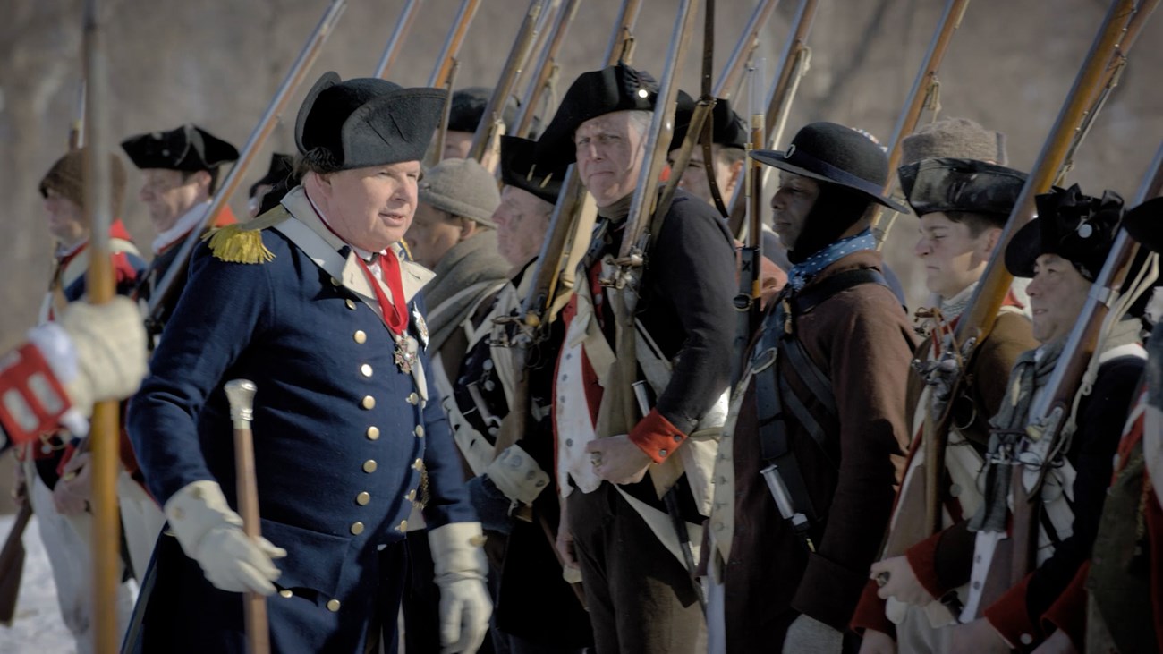 Baron von Steuben Drills Troops at Valley Forge soldiers stand at attention holding muskets and a large man in 18th century uniform stands in front