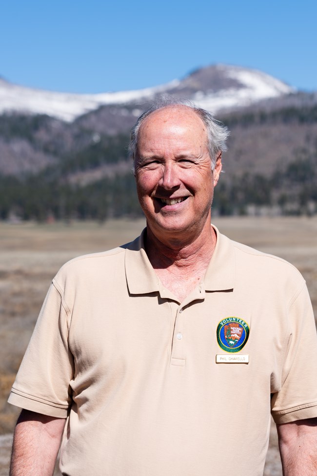 A man in a National Park Service volunteer uniform shirt smiles at us.