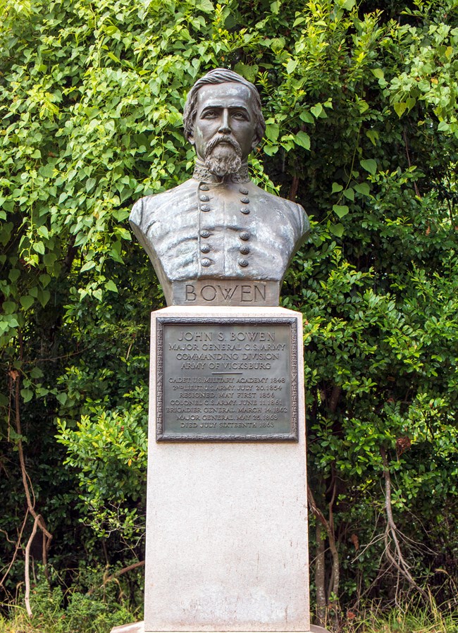 A bronze bust of a man in uniform sits atop a pedestal. Inscribed on the pedestal is a plaque that states the name and title of the man