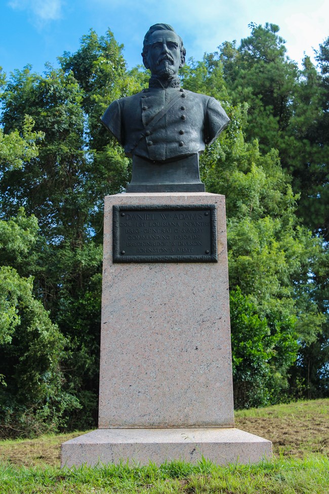 A bronze bust sculpture of a man in uniform sits on a granite pedestal with a small plaque with an inscription on it