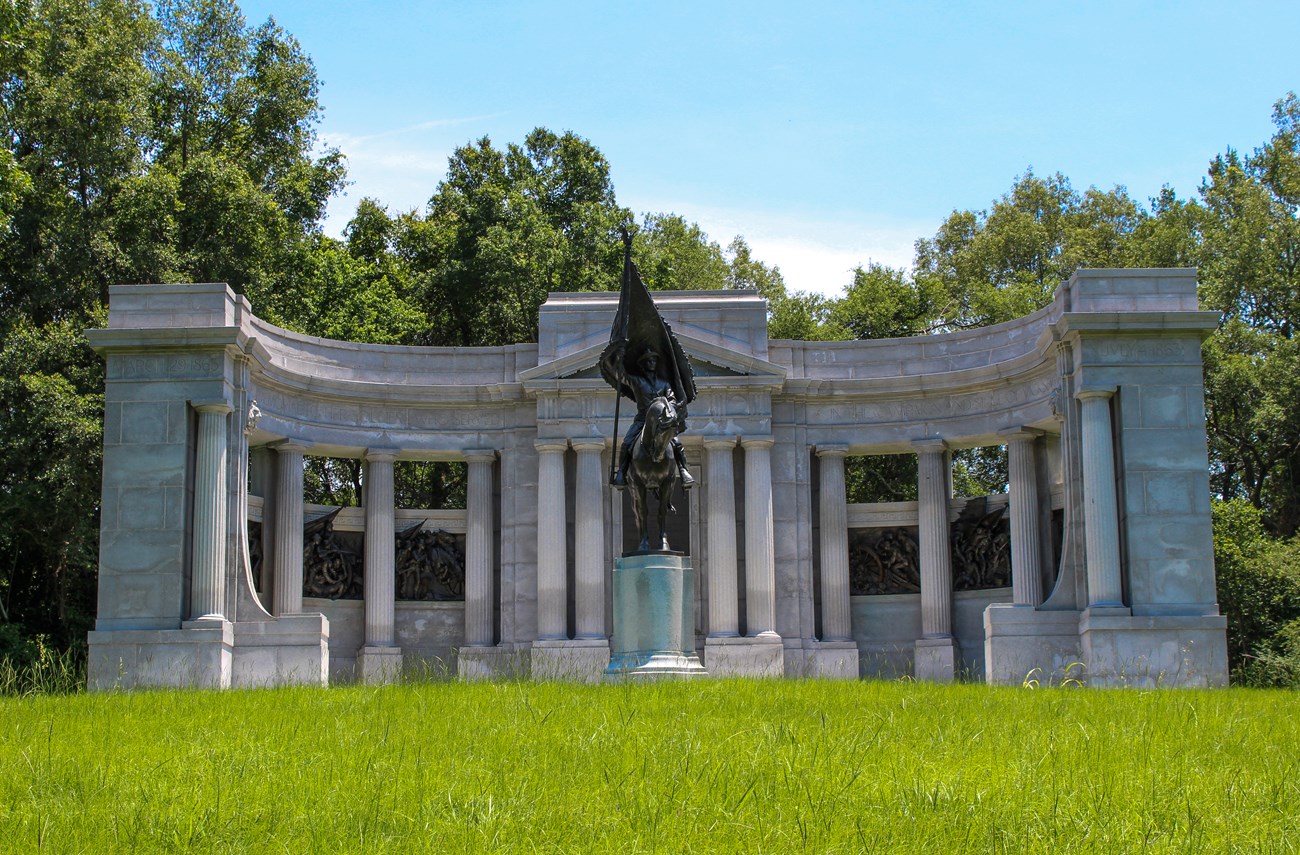 Tall granite pillars form a half circle around a tall bronze statue of a soldier riding a horse mounted on a granite pedestal.