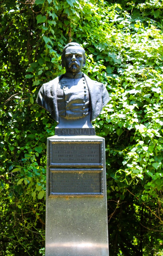 A bronze bust statue of a man dressed in Uniform mounted on a pedestal