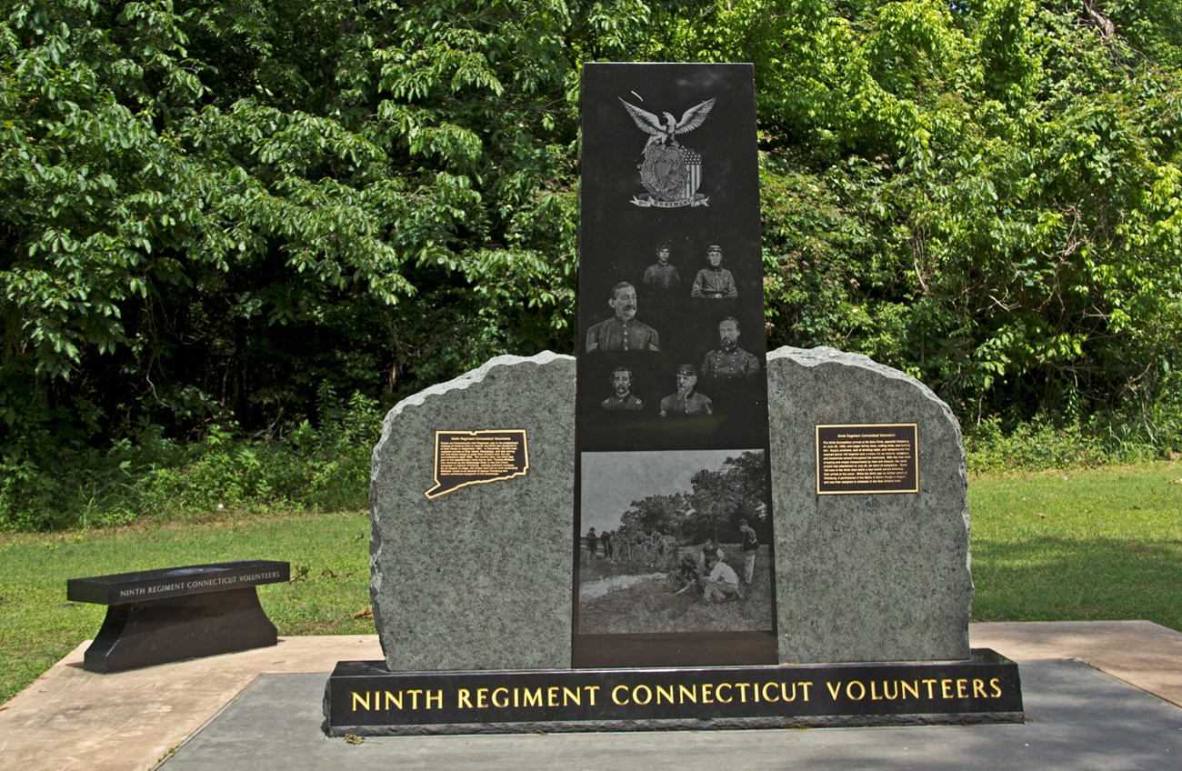 A tall vertical black slab with etchings of 6 individual portraits and a group image is placed between two large pieces of stone. Underneath reads Ninth Regimant Connecticut Volunteers.
