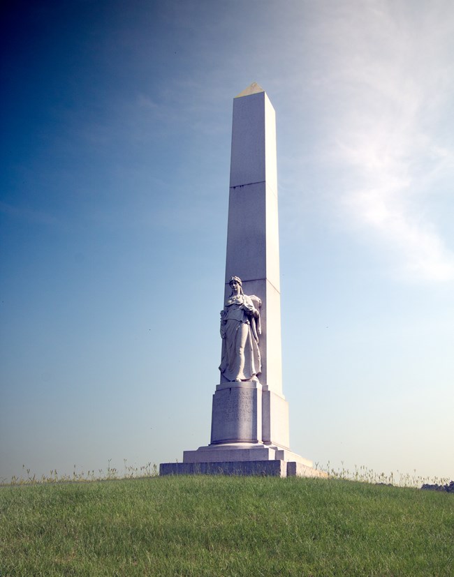 The Michigan Memorial which is a tall concrete column with a sculpture of a woman in a dress.