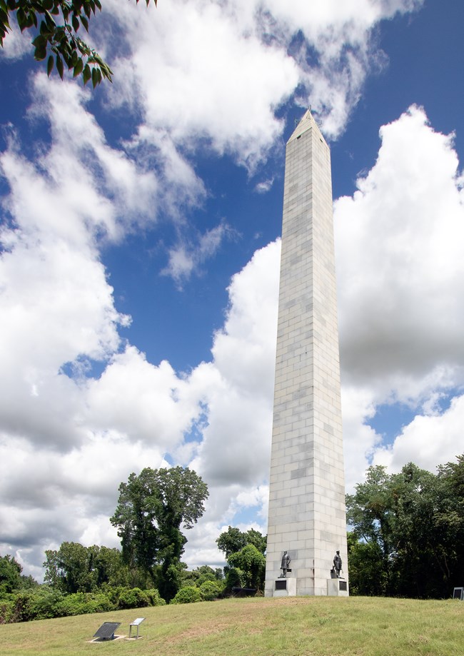 Tall vertical white monument with four bronze statues of four men