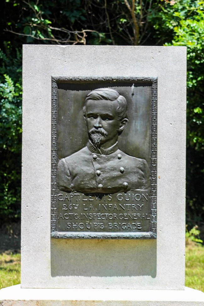 A bronze relief portrait of a man in uniform followed by a short inscription