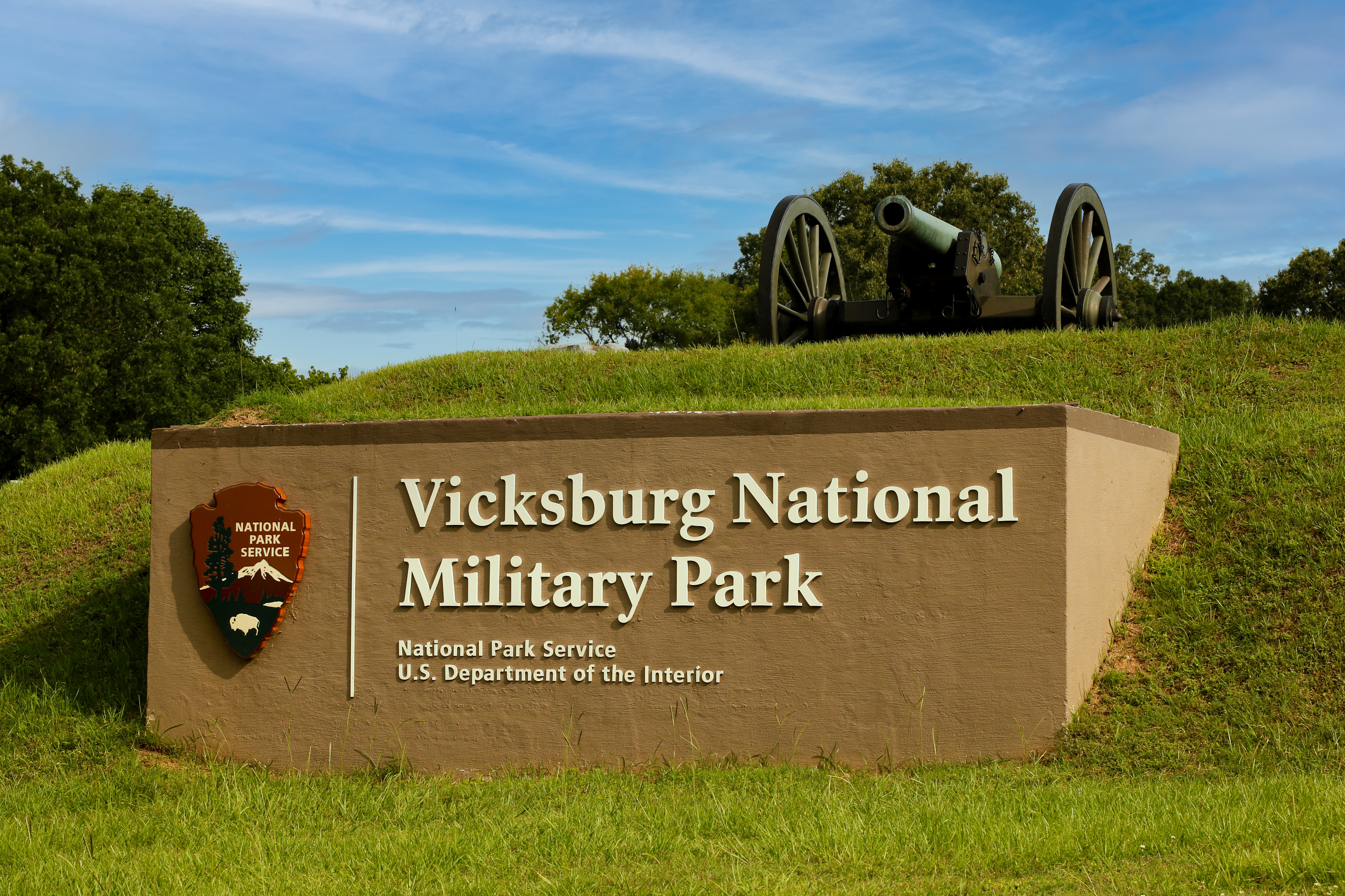 Grassy hill with cannon on top. Light brown cement sign in front with NPS Arrowhead and Vicksburg National Military Park