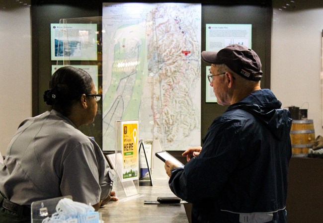 A park ranger assists a Visitor with a cell phone at the front desk in the visitor center.