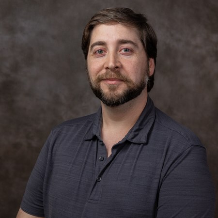 Image of the head and shoulders of a white man with brown hair and beard wearing a dark gray polo shirt