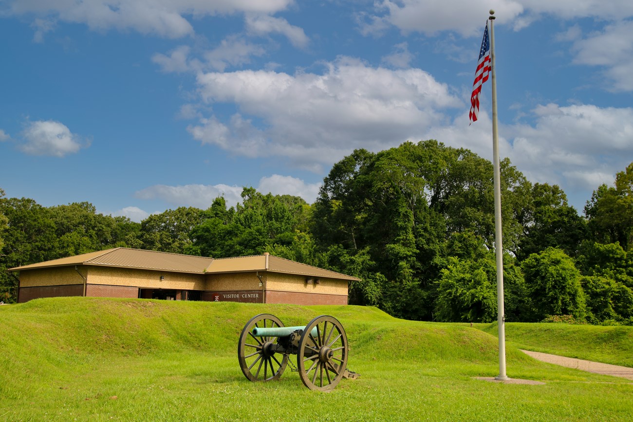 A historic cannon and flagpole with American Flag blowing in front of a building