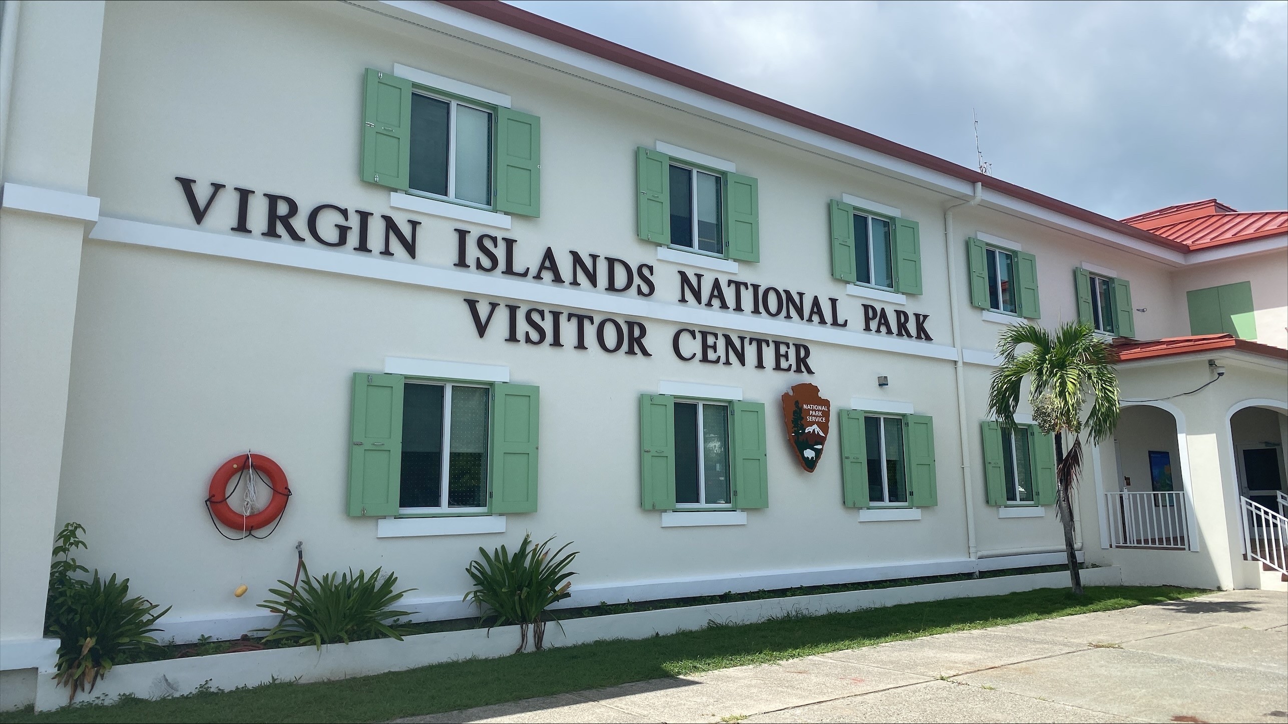 Image of the Virgin Islands National Park Visitor center building with green shutters and the NPS arrowhead.