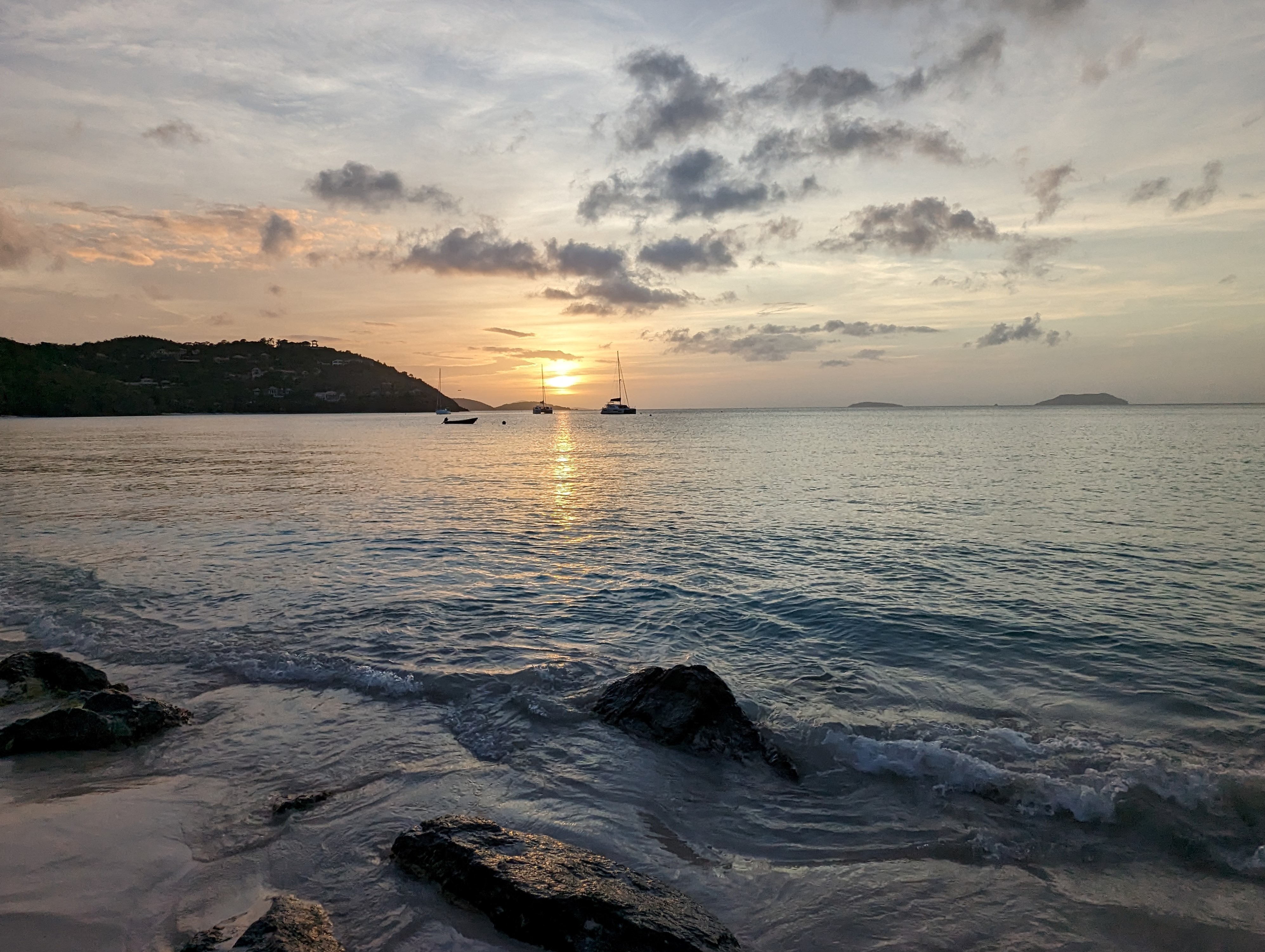 Image of the beach at Cinnamon Bay at sunset with boats in the distance.