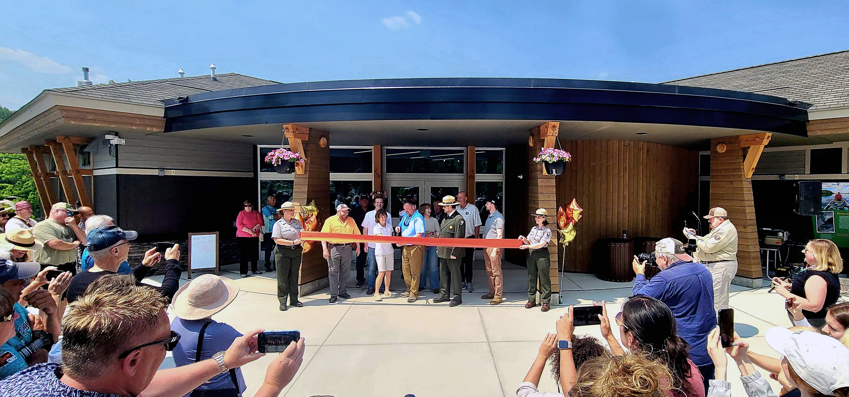 Photograph of crowd watching red ribbon be cut in front of building.