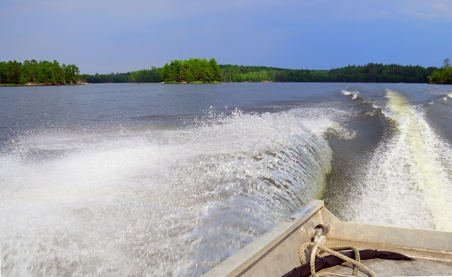 A boat cruises across a large scenic lake and leaves a large, blue wake behind it.