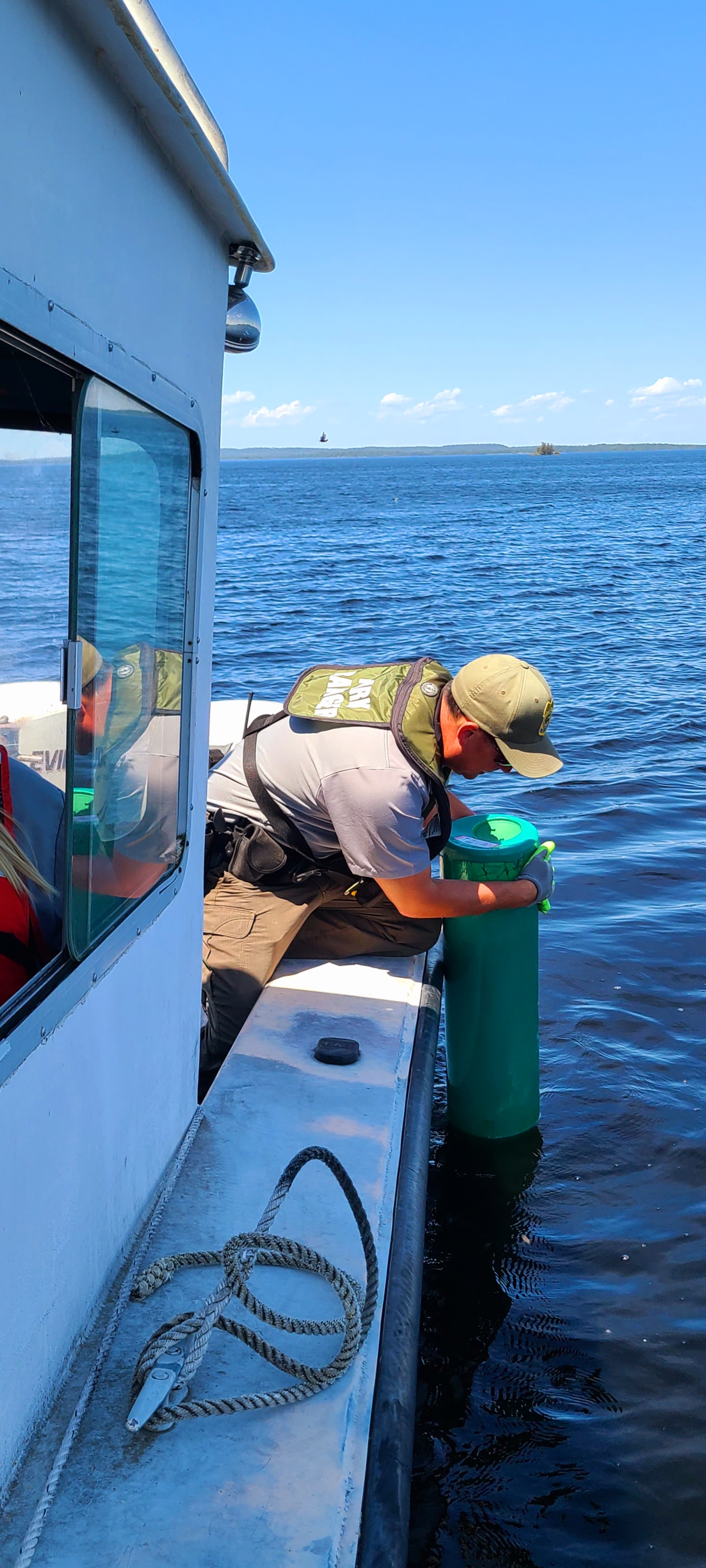 A Park Ranger reaches over the side of a boat to remove a buoy from Rainy Lake.