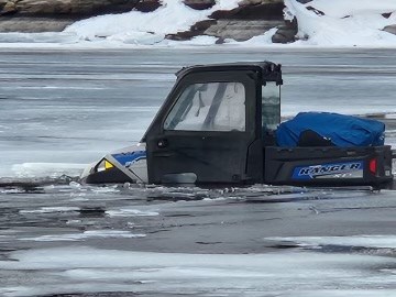 a two person utility vehicle is submerged in shallow water, after falling though the ice on a frozen lake.