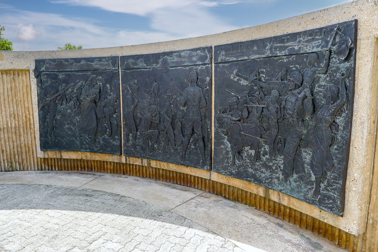A curved wall set with engraved metal panels showing scenes of the Battle of Guam
