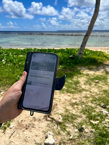 A phone open to the self-guided tour page for War in the Pacific National Historical Park. In the background is the beach and ocean.