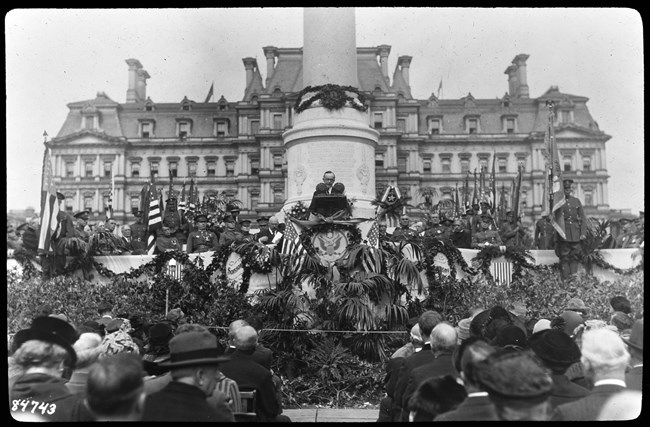 NARA 79-LS-03-C A man speaks from a lectern flanked by uniformed soldiers, flags, and bunting.