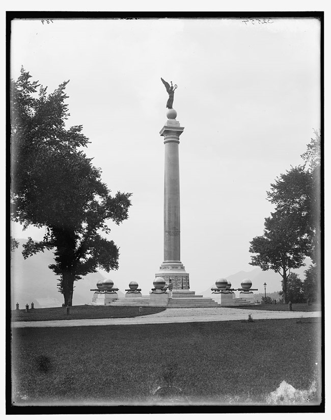 service-pnp-det-4a10000-4a16000-4a16700-4a16750v A statue of a winged figure holding a wreath aloft atop a tall column.