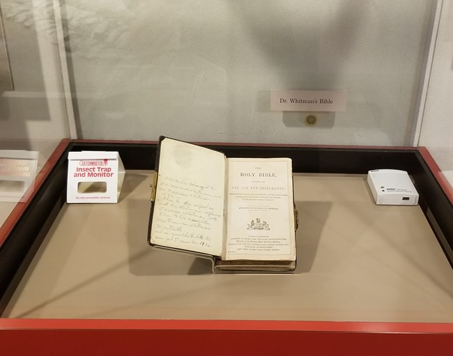 bible in a museum display case with a bug trap and a climate monitor