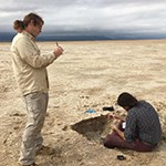 A man takes notes while another examines the ground