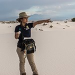 A woman points across white sand dunes.