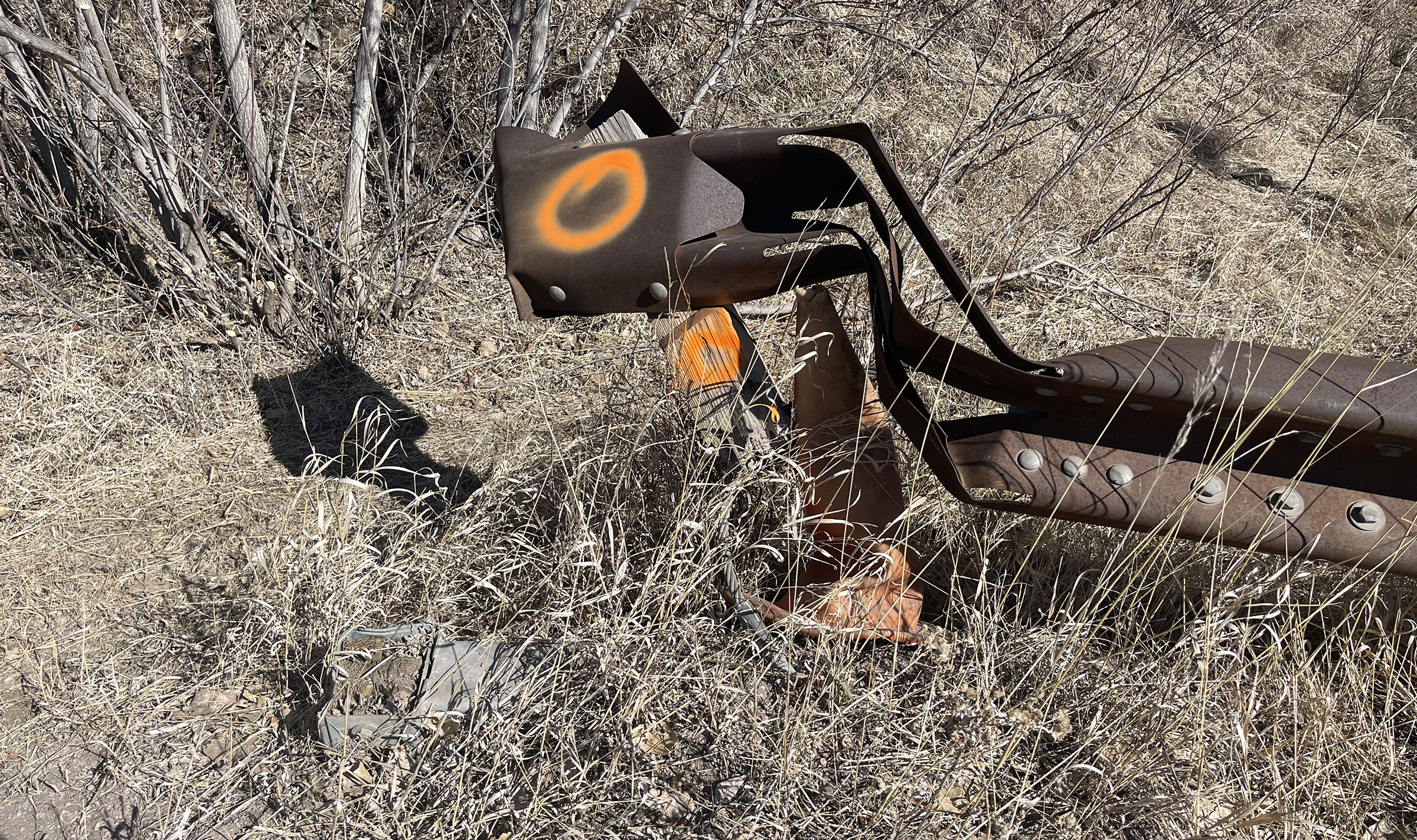 A mangled brown metal guardrail surrounded by prairie grass.