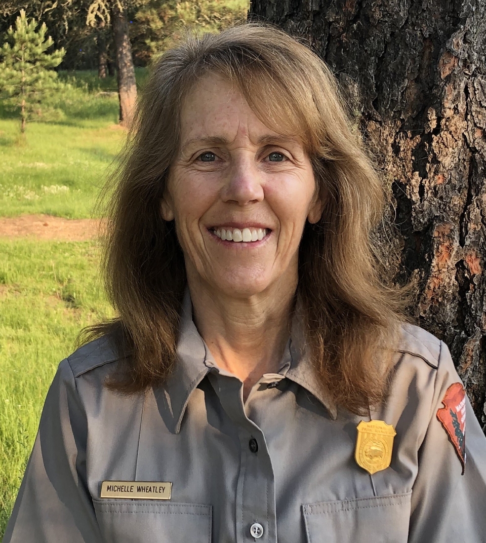 Female park ranger, Michelle Wheatley, in uniform looking at camera with a tree in the background.