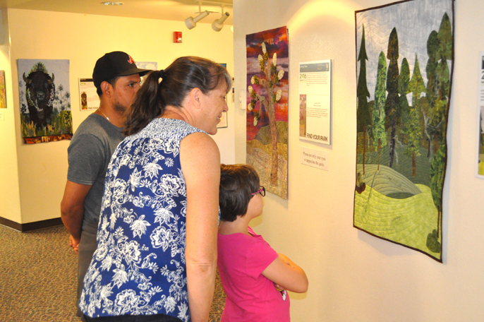 A family of three standing in front of one of the quilts.