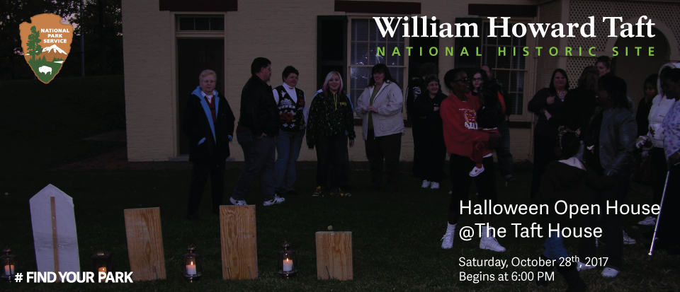 A group of people stand between a row of replica headstones and a house