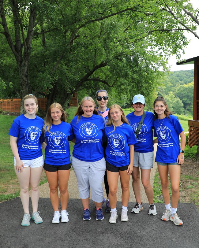 Seven women of varying generations pose wearing a blue shirt that reads "Volunteer Wolf Trap National Park for the Performing Arts"."