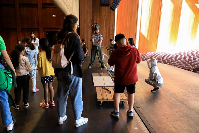 A ranger works with a group of students during a physics program on a stage.