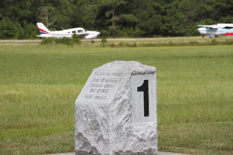 A granite marker in foreground and two airplanes in background.