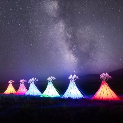 a row of illuminated and colorful teepees underneath a night sky