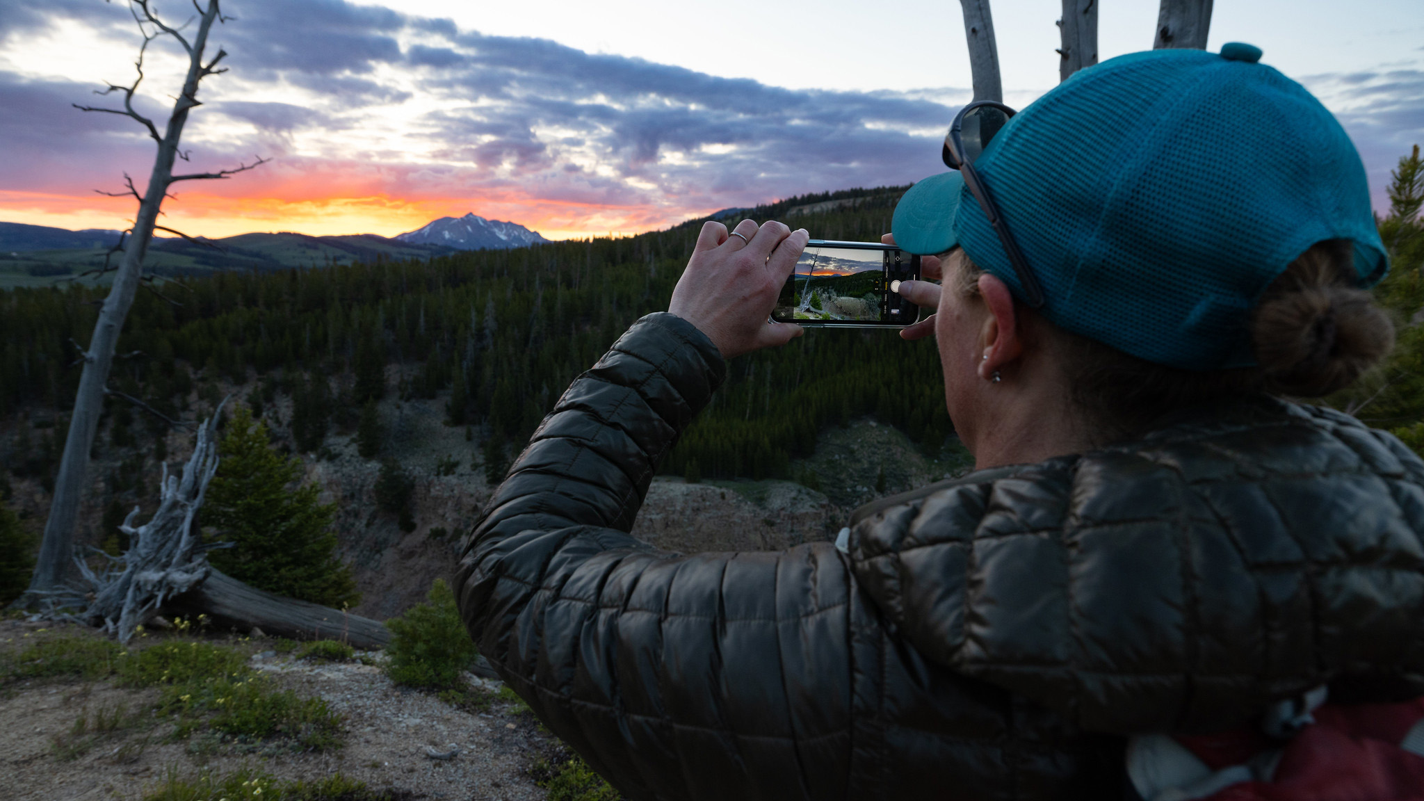 Person with a phone taking a photo of mountains and sunset