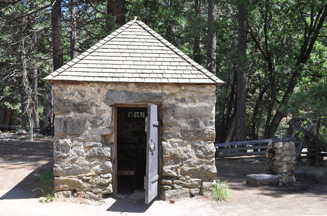 Se puede ver un catre viejo a través de la puerta abierta del recinto estrecho y de piedra con techo puntiagudo.