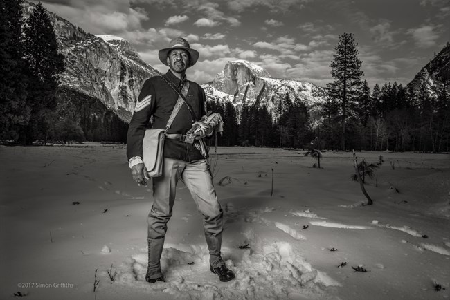 Ranger Shelton Johnson, portraying an early 20th century uniformed Buffalo Soldier, standing in a snowy meadow with Half Dome in the background