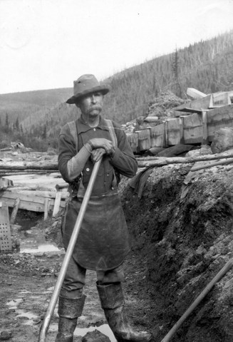 Yukon placer miner and cook John Rentfro takes a break from shoveling gravel from a cut-bank into sluice boxes, Eagle District, ca. 1904.