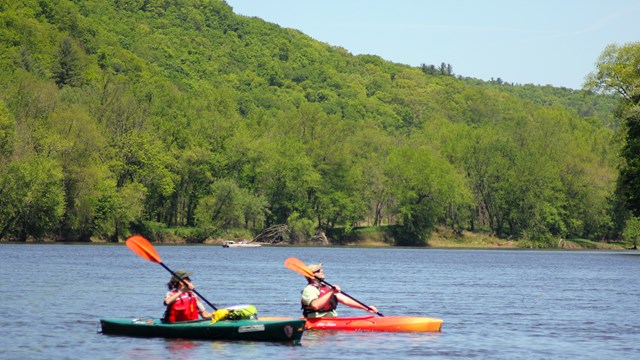 Two kayakers paddle along the Delaware river in summer