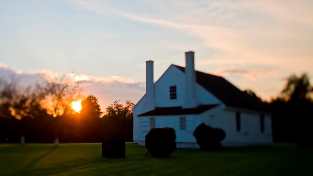 A small, white house with a-frame roof at sunset.