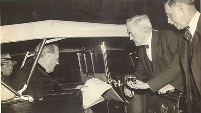 President sitting in a car signing a bill while three men watch