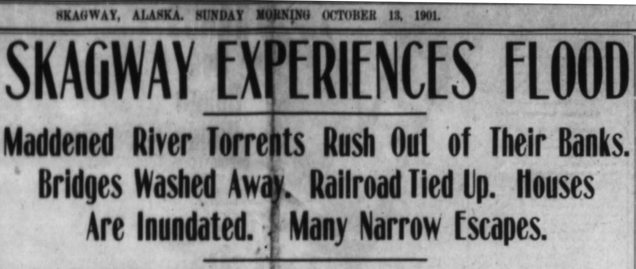 Newspaper headline reads "Skagway experiences flood: maddened river torrents rush out of their banks. Bridges washed away. Railroad tied up. Houses are inundates. Many narrow escapes."
