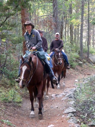 Photo of visitors riding horses along a trail through the forest.